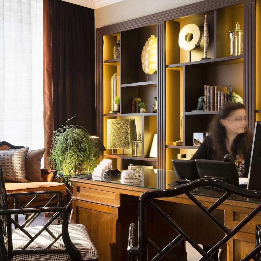 Un hall de hotel con un sofá, sillas, un mostrador de recepción y una estantería con diversos objetos.