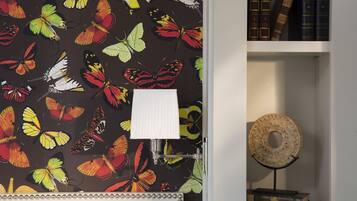 Una habitación con un papel tapiz estampado con mariposas, una lámpara blanca y un objeto decorativo redondo sobre un pedestal.