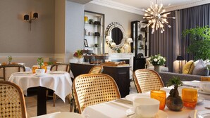 A hotel dining area with tables set for breakfast, wicker chairs, a mirror, and a chandelier. - Hotel Monge (Paris)