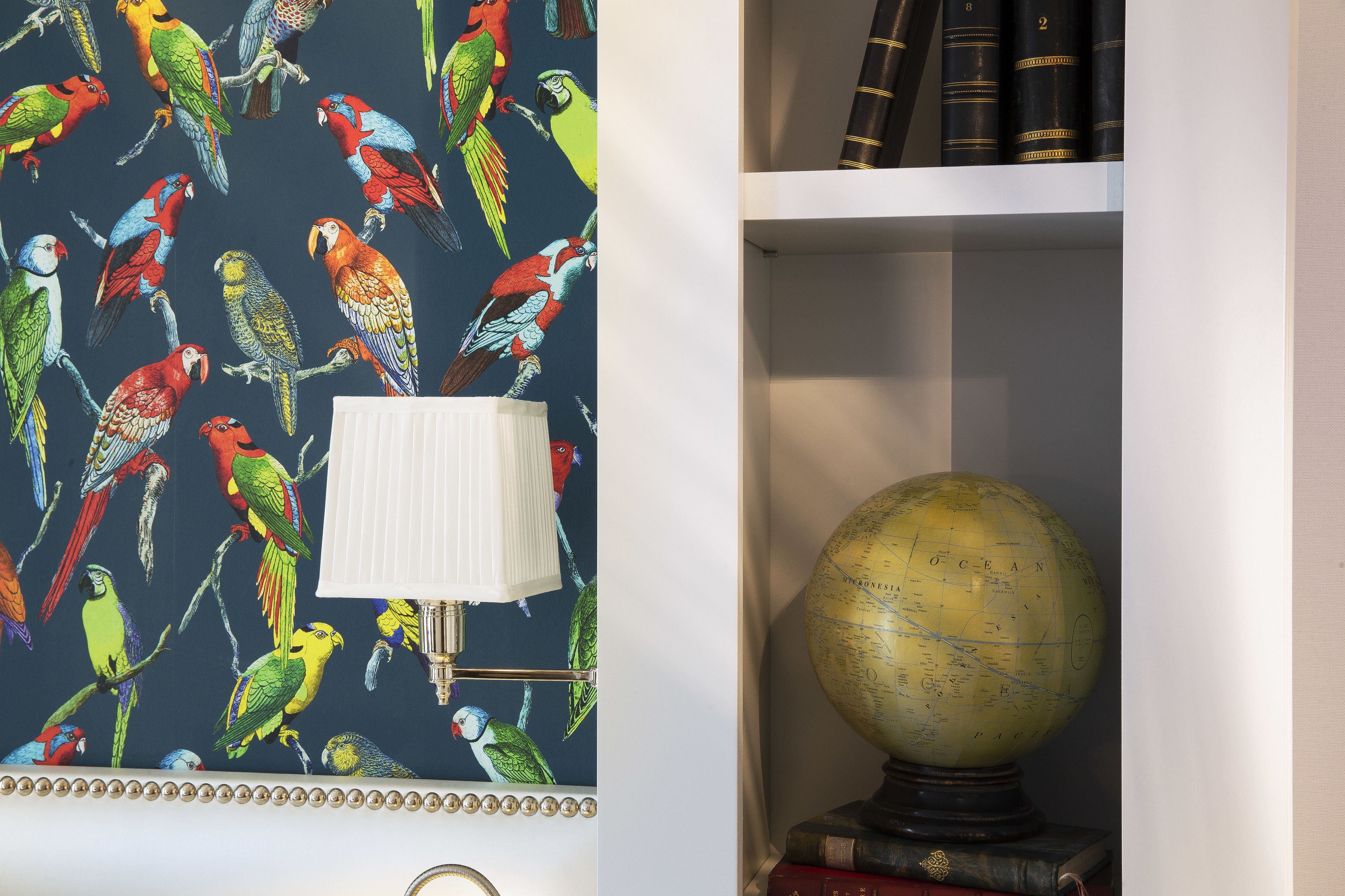 Eine Wand mit Tapete mit Papageienmuster, ein Globus auf einem Stativ und eine Lampe.