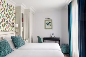 Una habitación de hotel con una cama grande, una mesita de noche, un escritorio, una silla, una ventana con cortinas y una pared decorada con un estampado de pájaros.