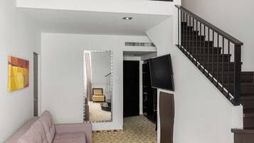 A multi-level living space with a staircase, a sofa, a television, and a mirror.
