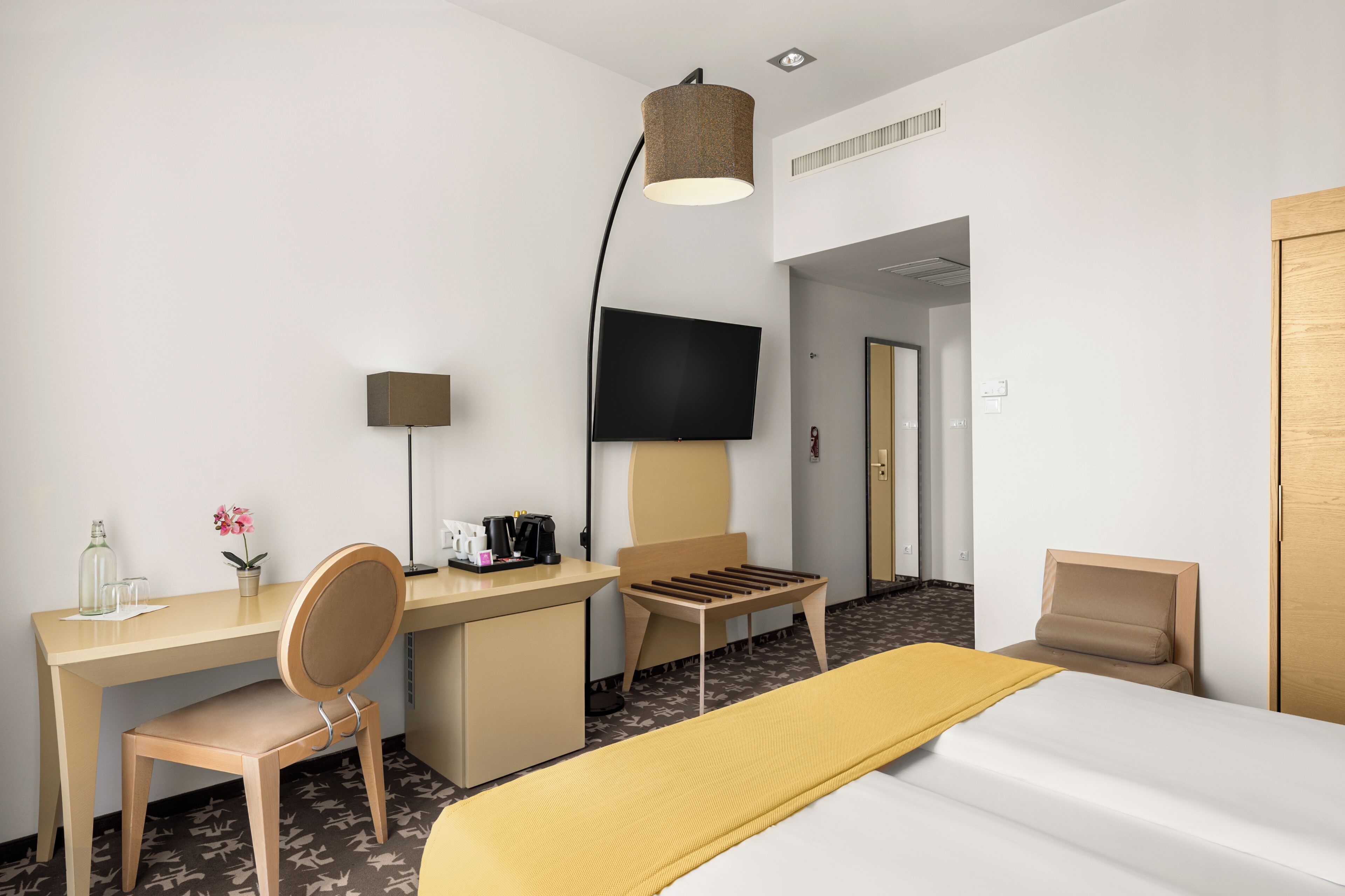 A hotel room with a bed, desk, chair, TV, and a lamp.