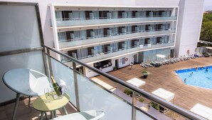 Un balcón de hotel con piscina, sillones de descanso y una mesa con una botella de champán.