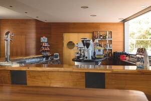 Zona de bar con una máquina de café, estantes con botellas y un ventanal con luz natural.