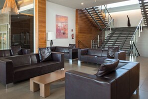A modern lobby with leather sofas, a wooden coffee table, and a staircase with glass railings. - RVHotels Nautic Park (Castell-Platja d'Aro)