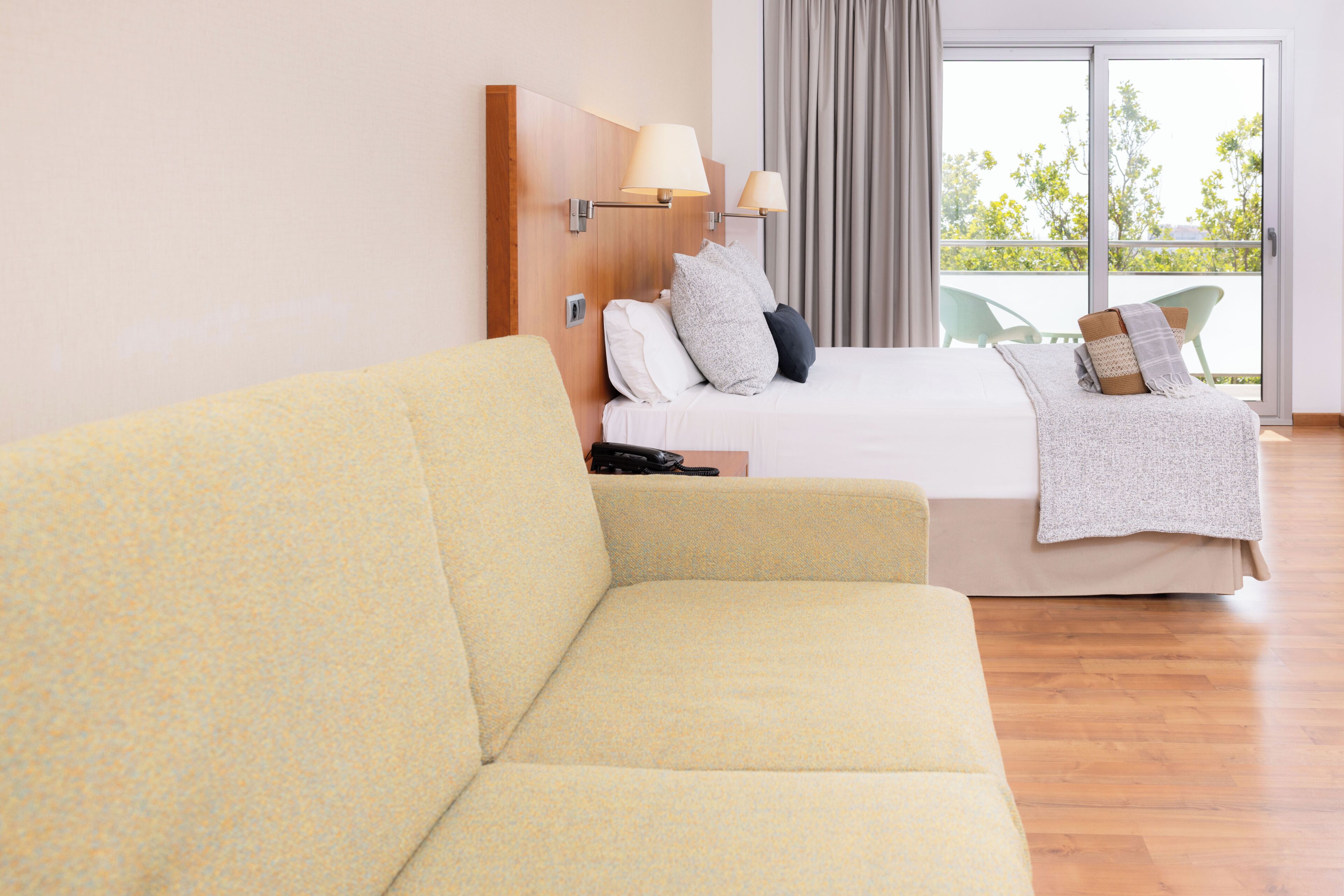 A hotel room with a bed, a sofa, a window with curtains, and a view of trees.