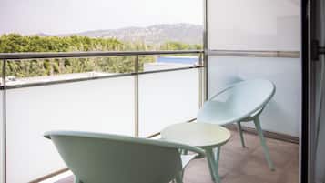 Un balcón con dos sillas, una mesa, un ventanal de vidrio y vistas a zonas verdes y colinas al lejano.