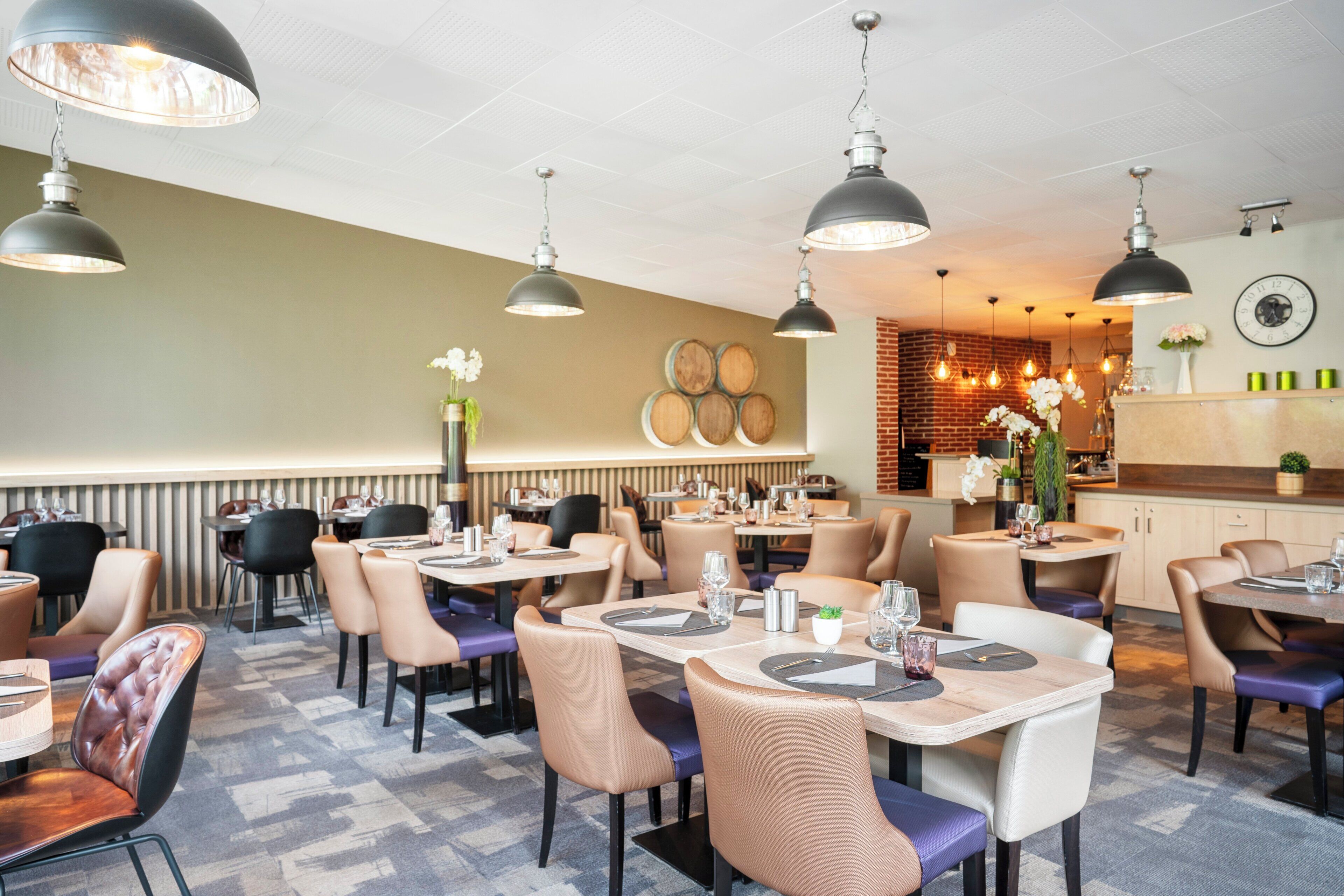 A restaurant with multiple tables and chairs, pendant lighting, and a brick wall in the background.