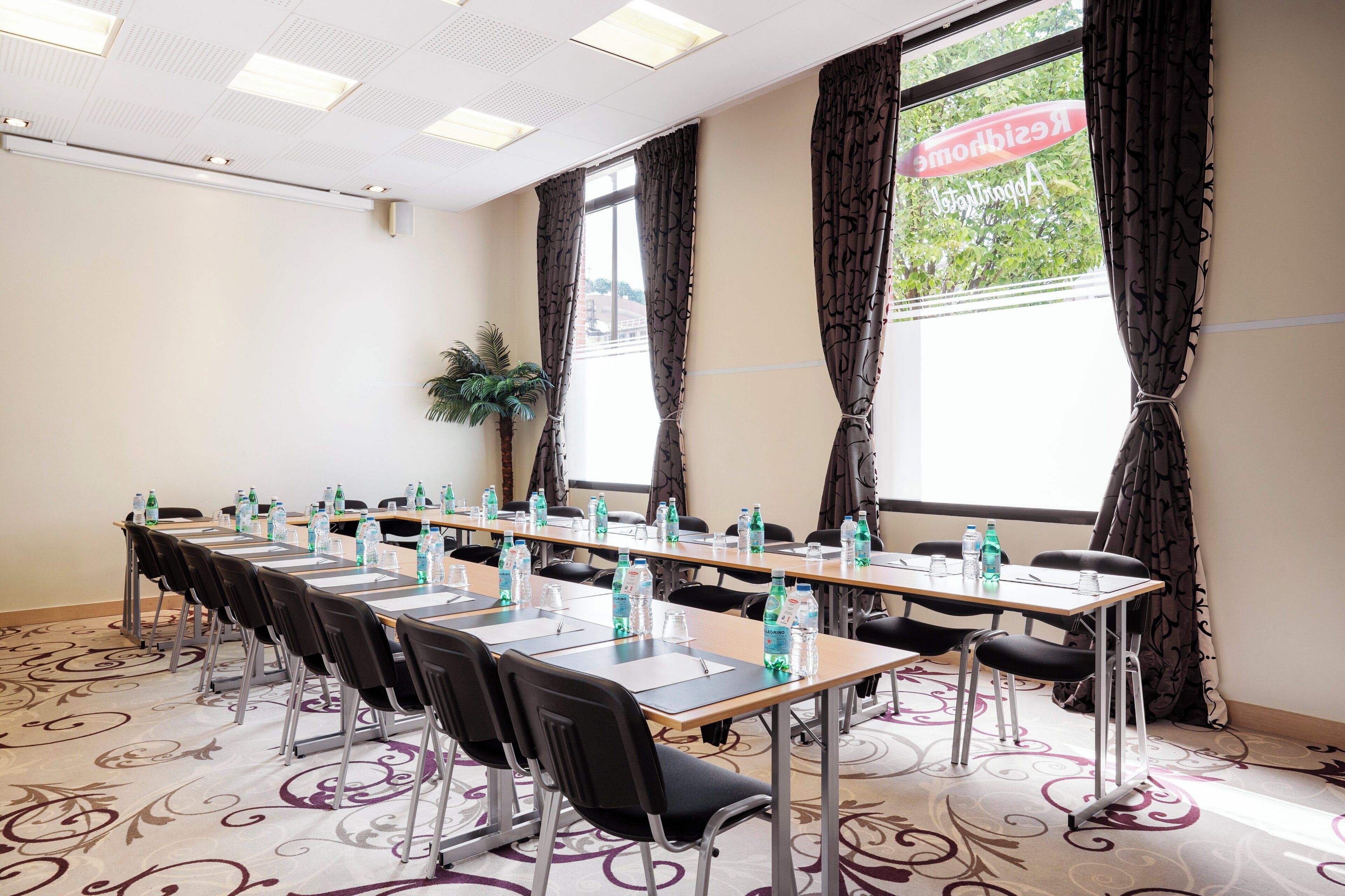 A conference room with a long table, chairs, water bottles, and a potted plant.