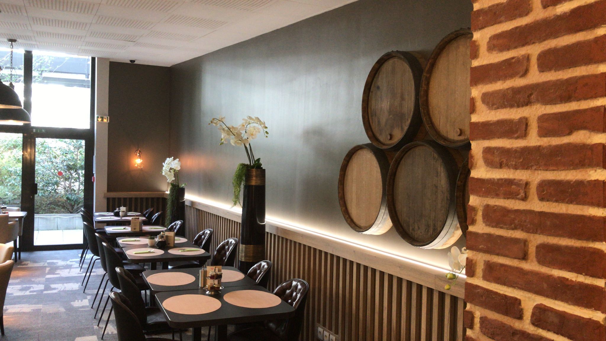 Een restaurantinterieur met tafels, stoelen en een bakstenen muur met houten vaten.