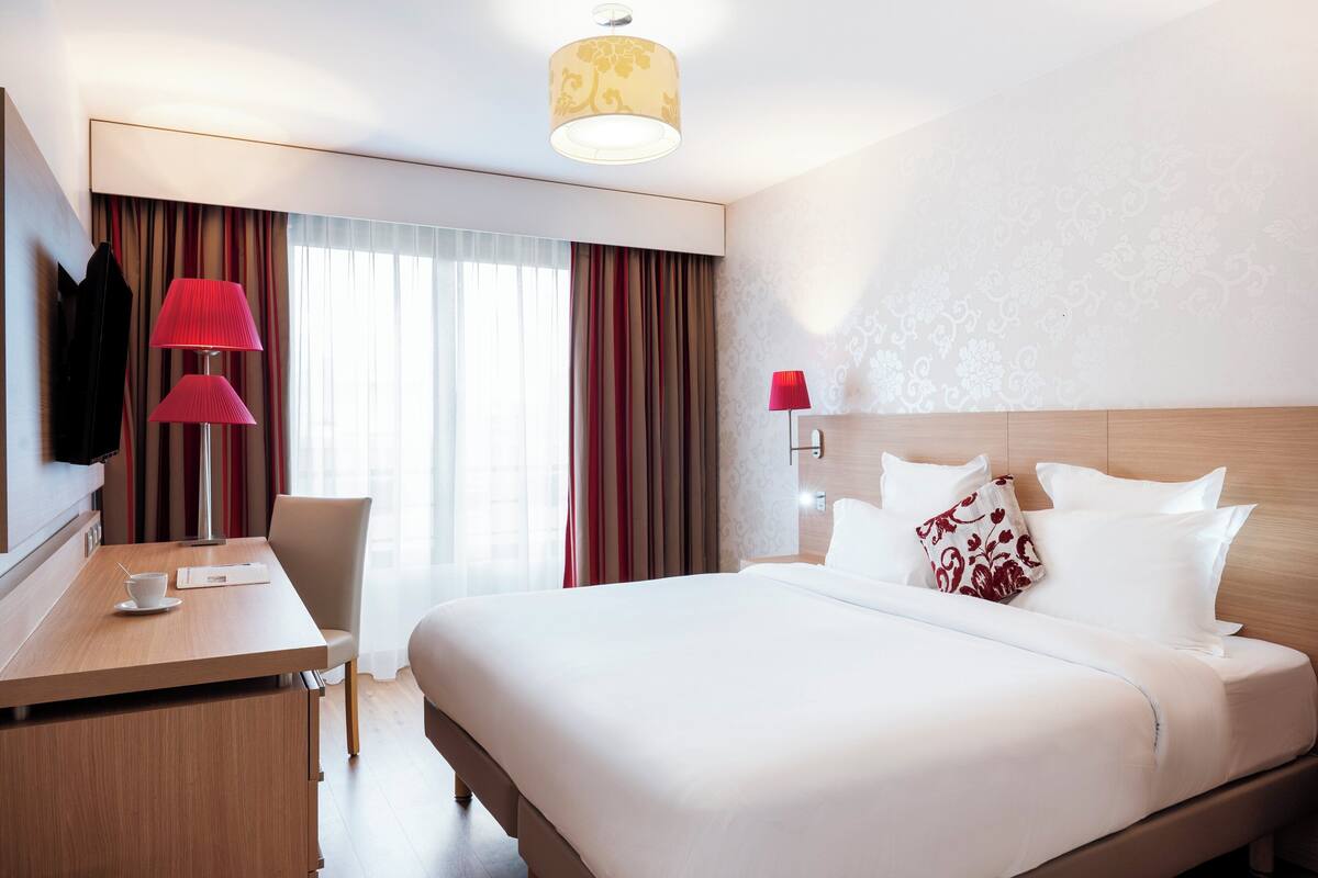 A hotel room with a bed, a desk with a chair, a TV, and a lamp.