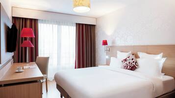 Een hotelkamer met een bed, een bureau met stoel, een televisie en een lamp.