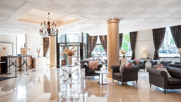 Um hall amplo com um candelabro, assentos confortáveis e grandes janelas com vista para a cidade.