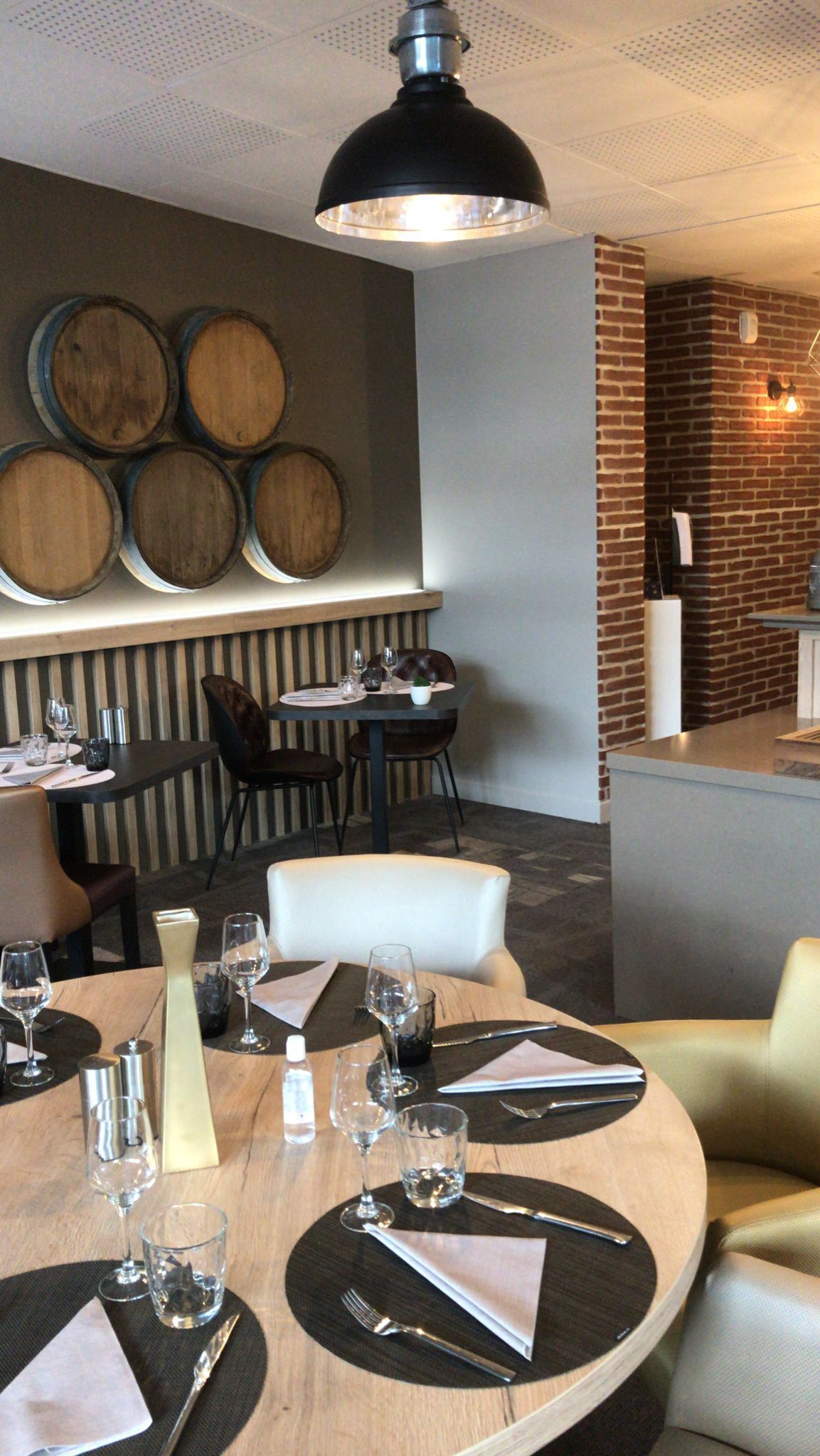 Ein Restaurantinneres mit runden Tischen, einer schwarz-weißen Streifenwand und Holzfässern an der Wand.