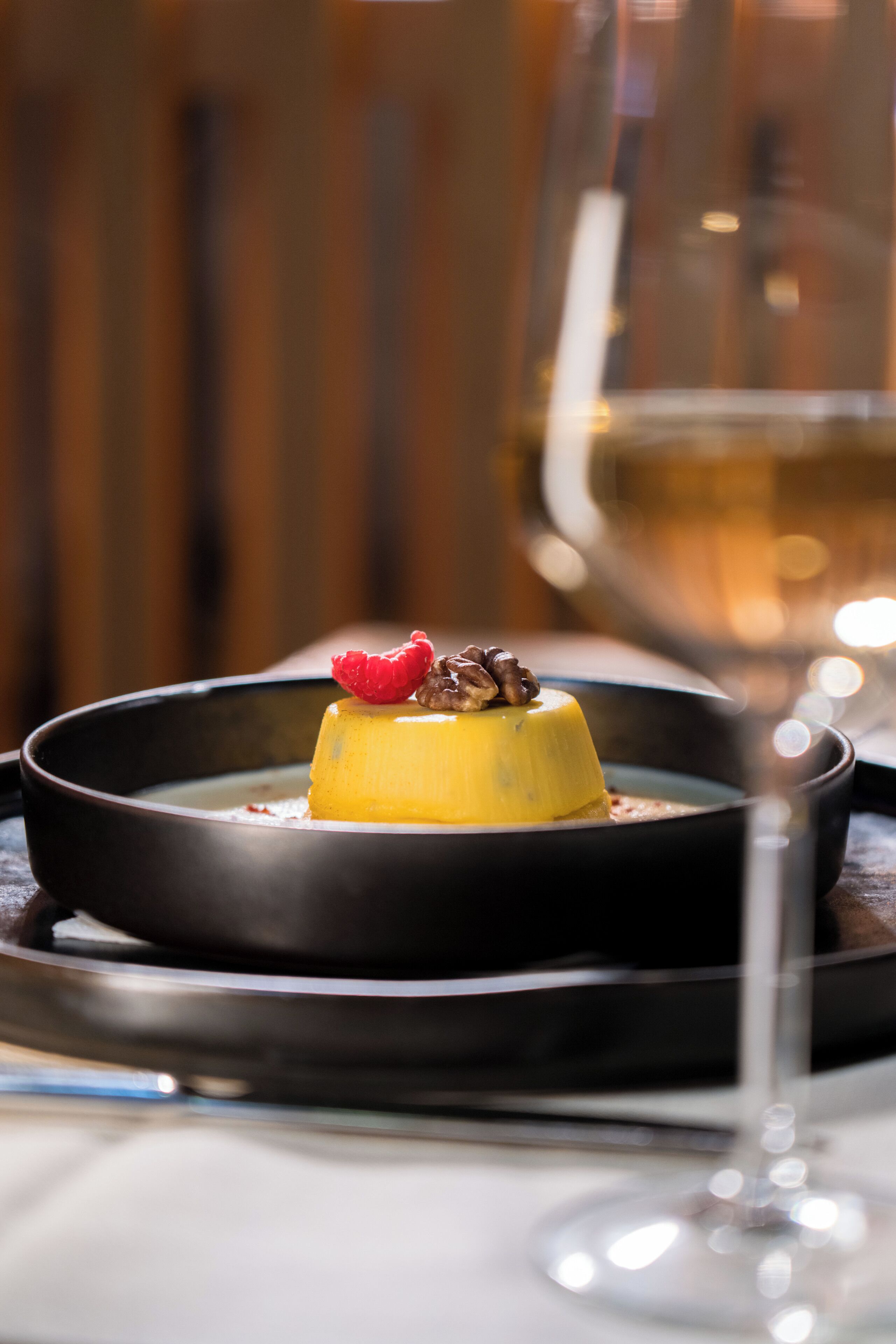 Un postre en un plato, con una copa de vino al fondo.