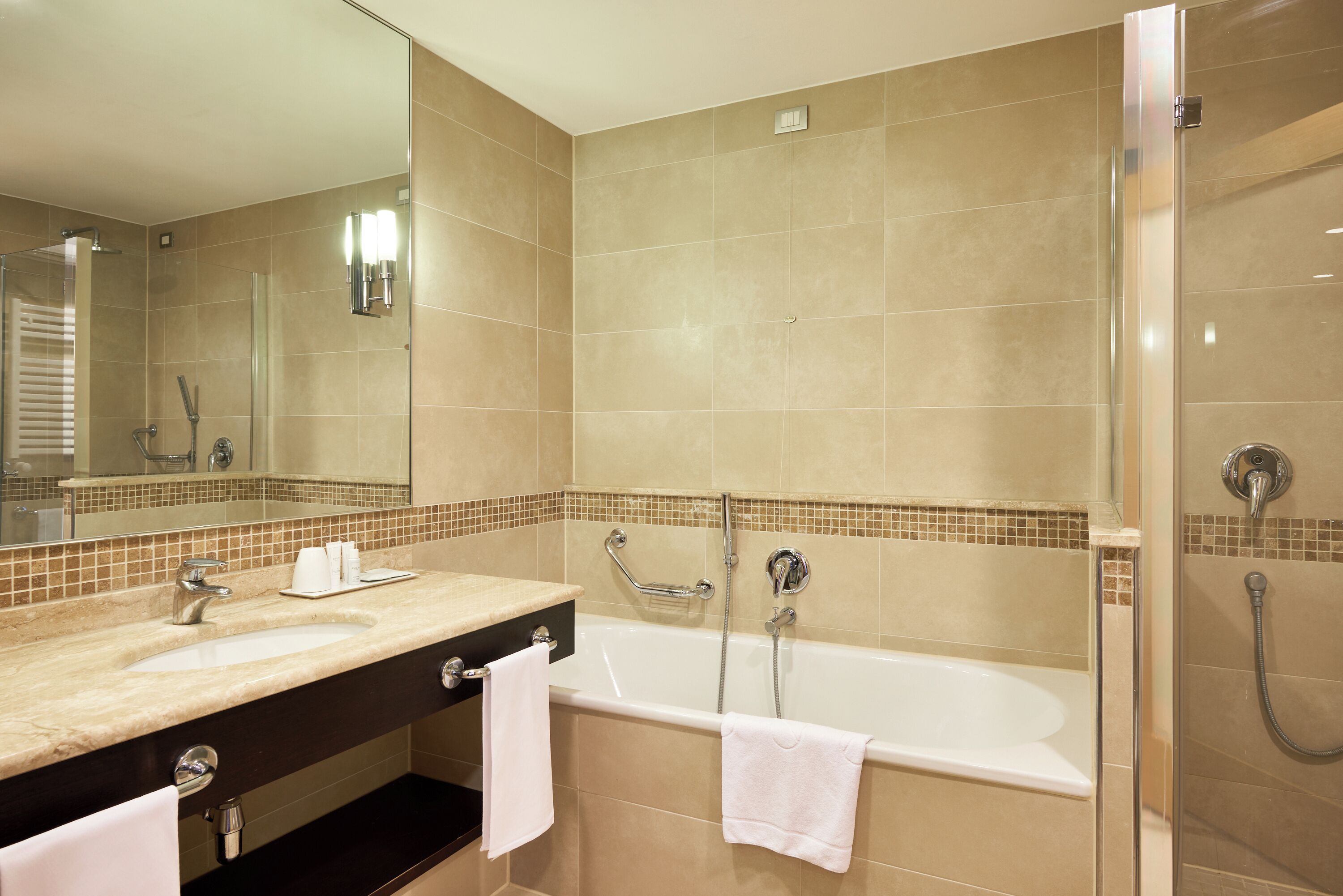 A modern bathroom with a large mirror, two sinks, a bathtub, and a shower.