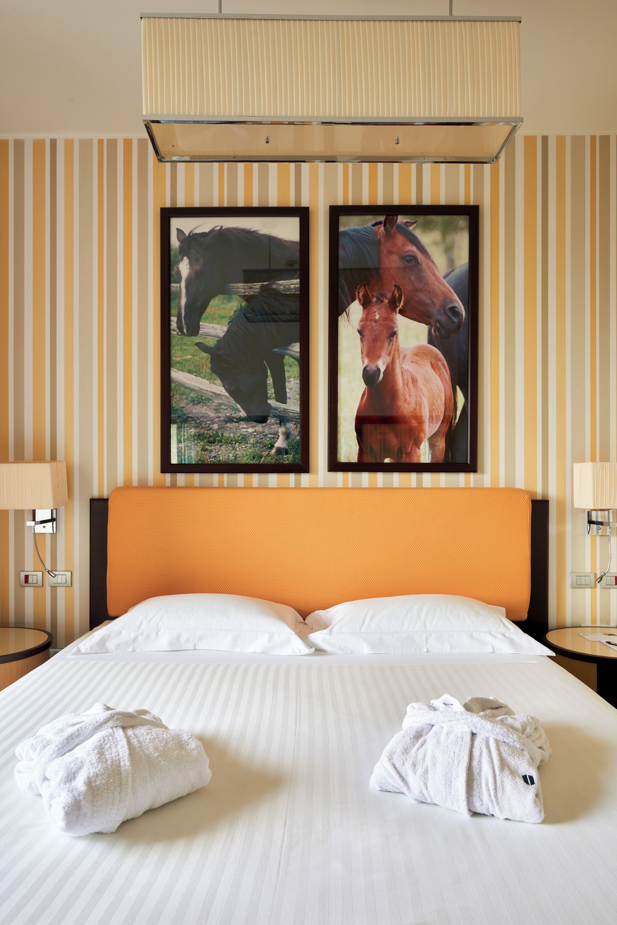 Ein Hotelzimmer mit einem großen Bett, zwei gerahmten Bildern von Pferden und zwei Nachttischlampen.