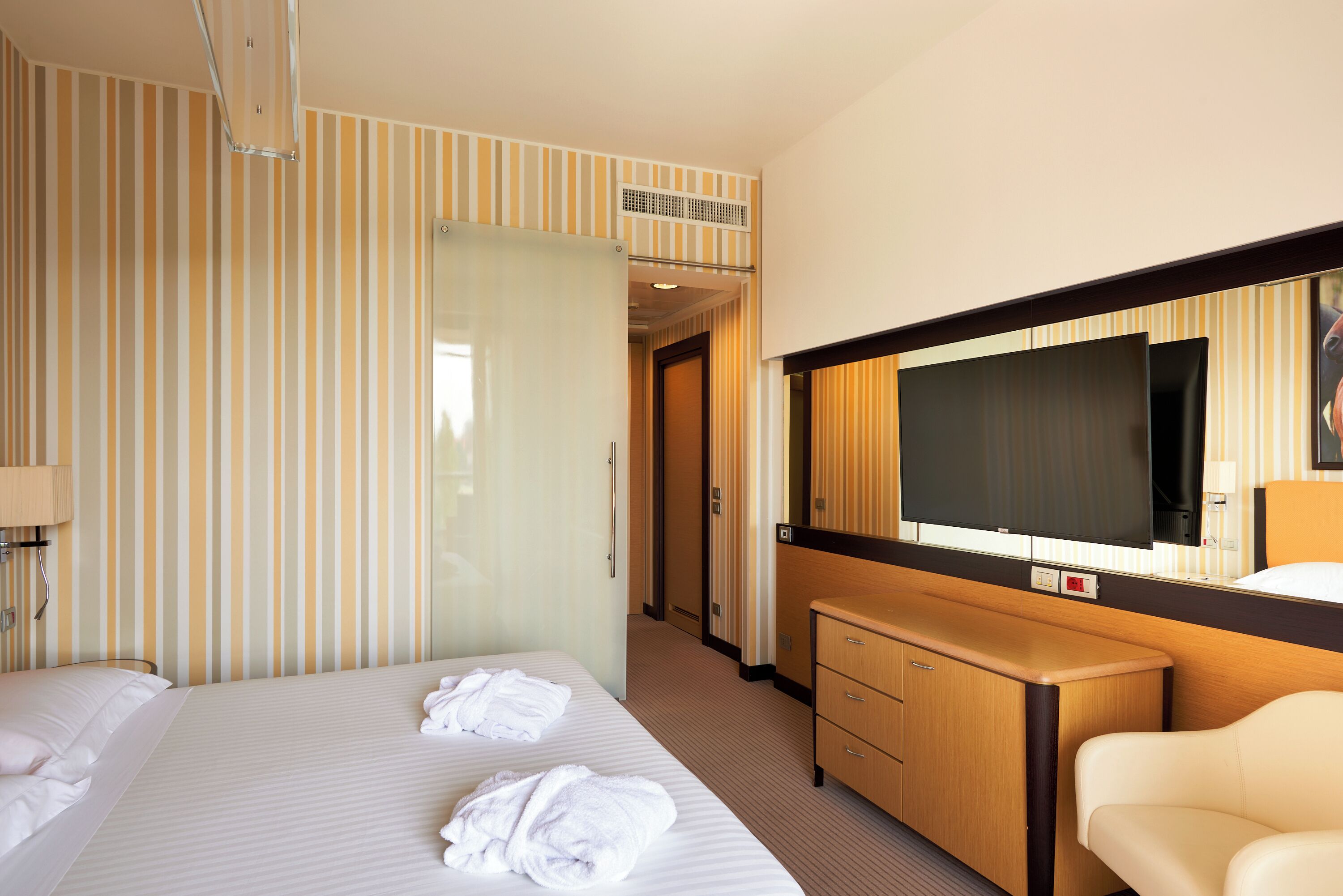 A hotel room with a bed, a TV, a dresser, and a mirror.