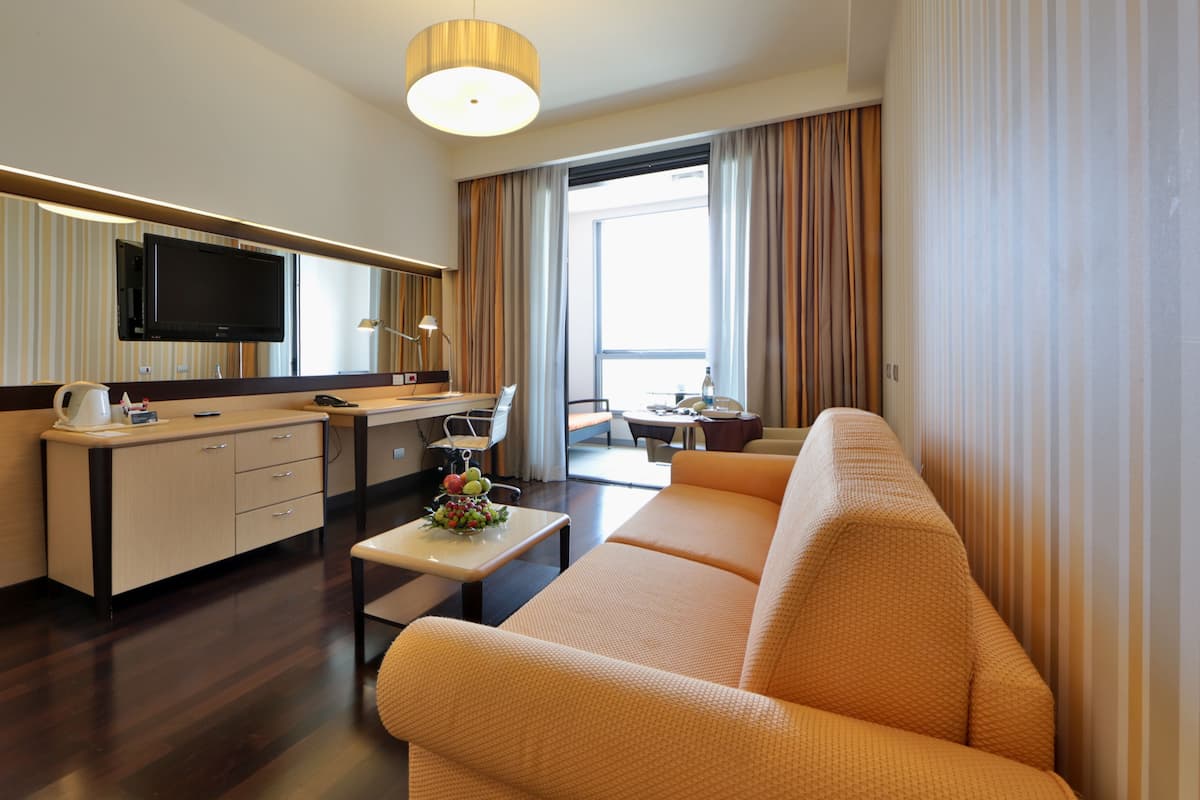 Una habitación de hotel moderna con sofá, una mesa de comedor, televisor y kitchenette.