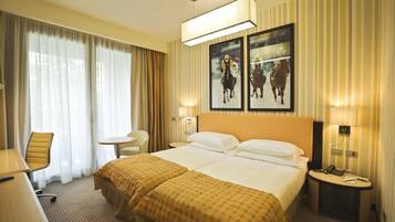 A hotel room with a large bed, a desk, a chair, and a small table. There are two framed pictures on the wall.
