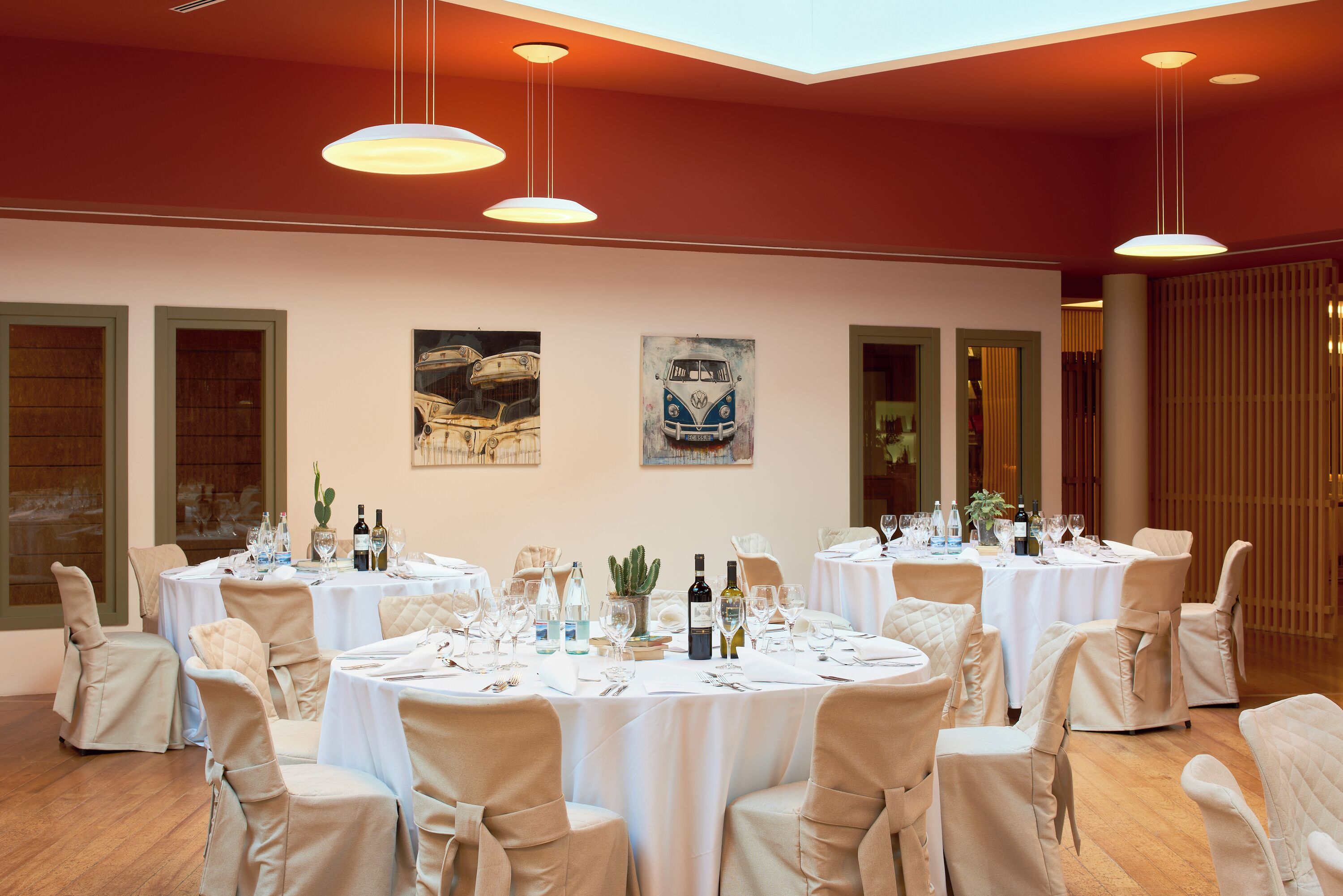 A dining area with round tables set for a meal, chairs, and hanging pendant lights.
