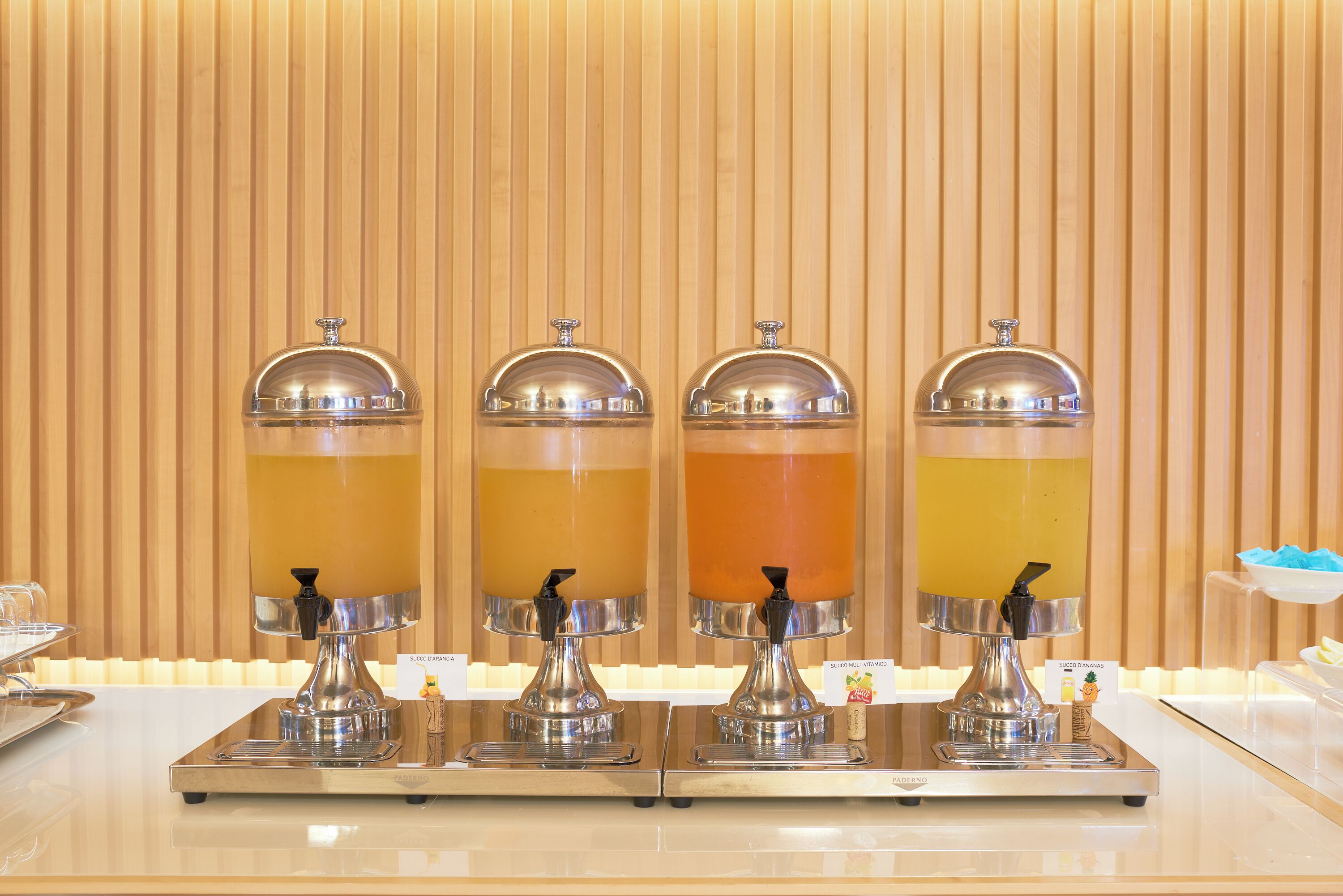 A beverage station with four dispensers against a wooden backdrop.