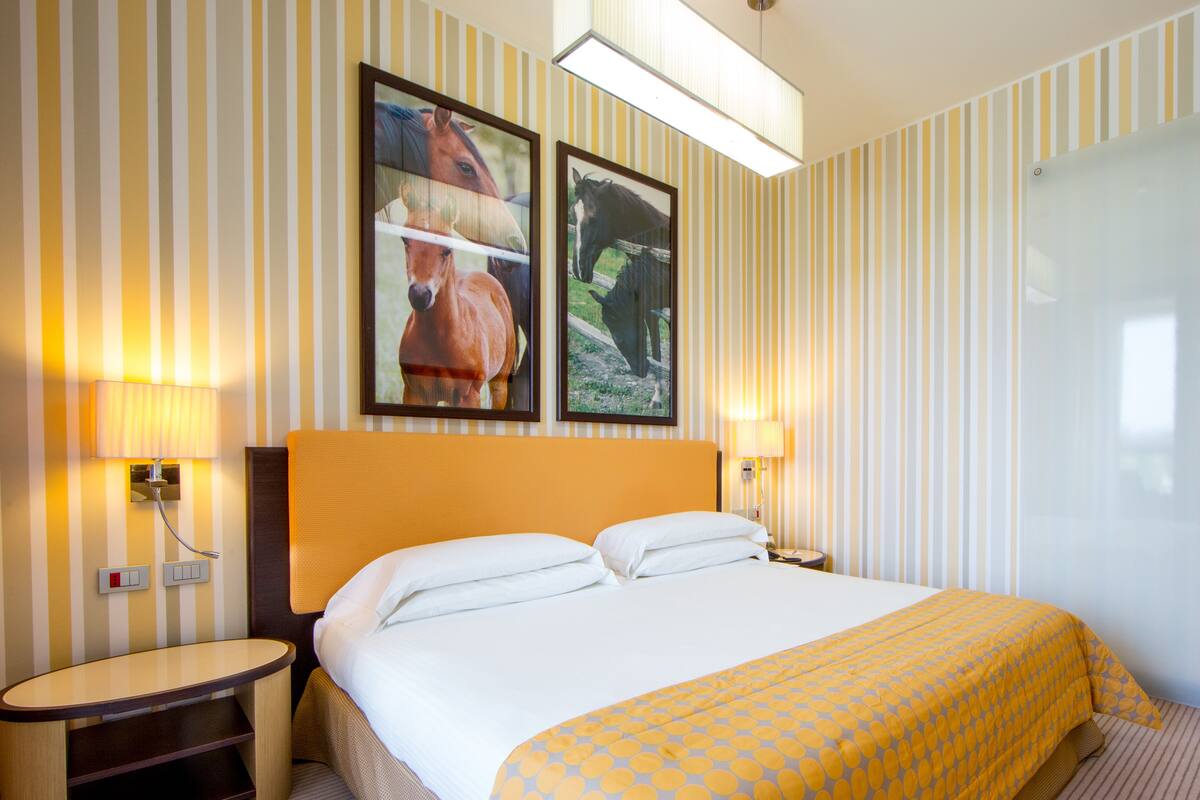 A hotel room with a large bed, two bedside lamps, a nightstand, and two framed pictures on the wall.