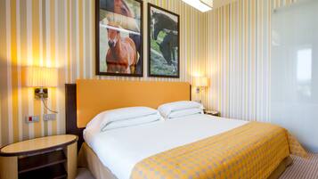 Una camera d'albergo con un letto grande, due lampade sui comodini, un tavolino da notte e due quadri appesi alla parete.