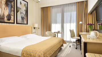 A hotel room with a large bed, a desk with a chair, a small table, and two framed horse pictures on the wall.