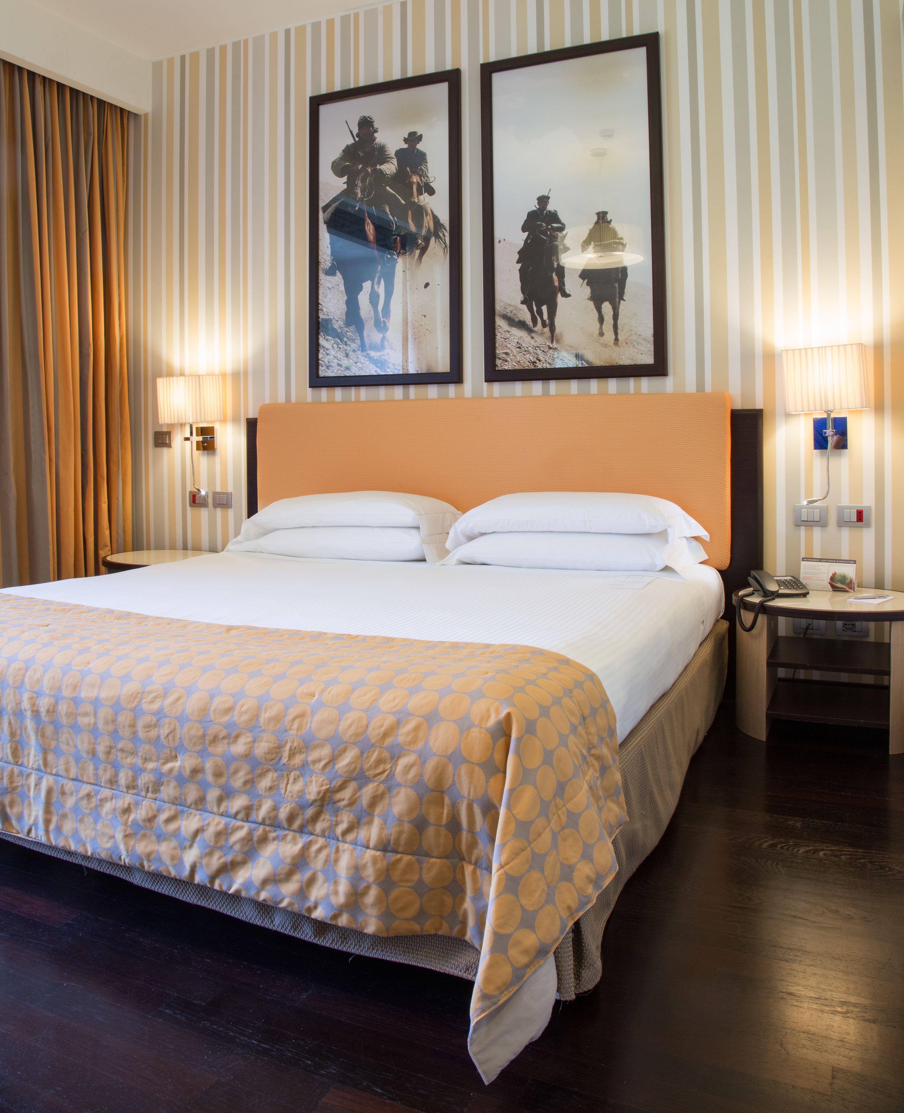 Una habitación de hotel con una cama grande, dos lámparas fijadas a la pared y dos cuadros enmarcados.