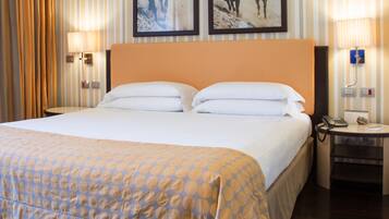 Una habitación de hotel con una cama grande, dos lámparas fijadas a la pared y dos cuadros enmarcados.