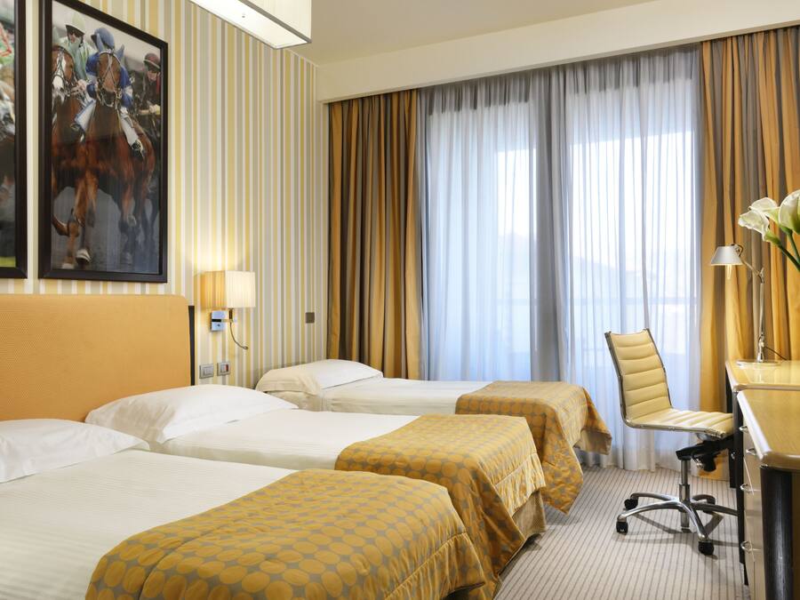A hotel room with two beds, a desk, a chair, and a large window with curtains.