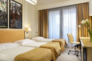 Habitación de hotel con dos camas, un escritorio, una silla y un ventanal grande con cortinas.