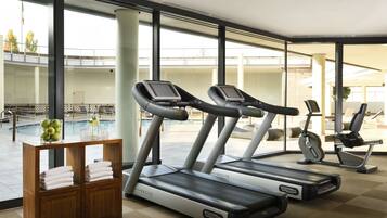 Una palestra con tapis roulant, una cyclette e una zona piscina visibile attraverso ampie finestre.