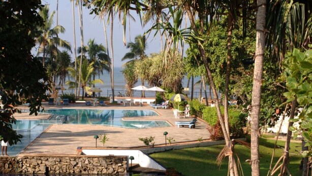 Un área de piscina con varias piscinas, rodeada de palmeras y un muro de piedra.