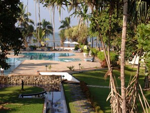A pool area with multiple swimming pools, surrounded by palm trees and a stone wall. - Villa Ocean View (Wadduwa)