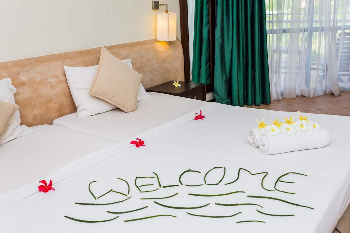 Habitación de hotel con cama, almohadas, mesita de noche, lámpara y ventana con cortinas.