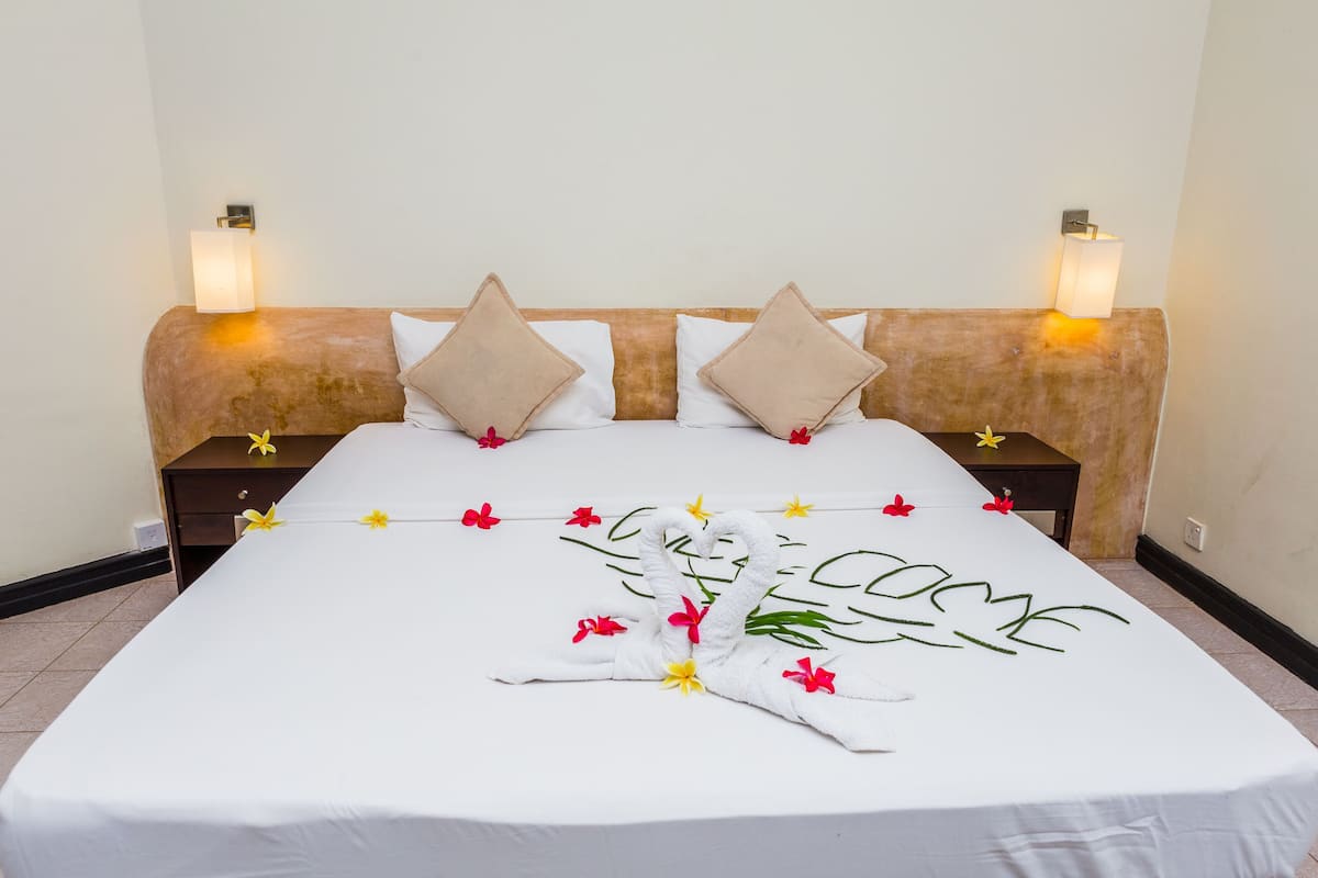 Una cama bien hecha con una colcha blanca, dos almohadas y arreglos florales decorativos.
