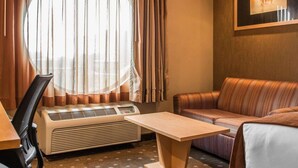 A hotel room with a large window, a sofa, a small table, and a desk with a chair.