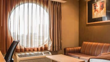 Habitación de hotel con un ventanal grande, un sofá, una mesita pequeña y un escritorio con una silla.