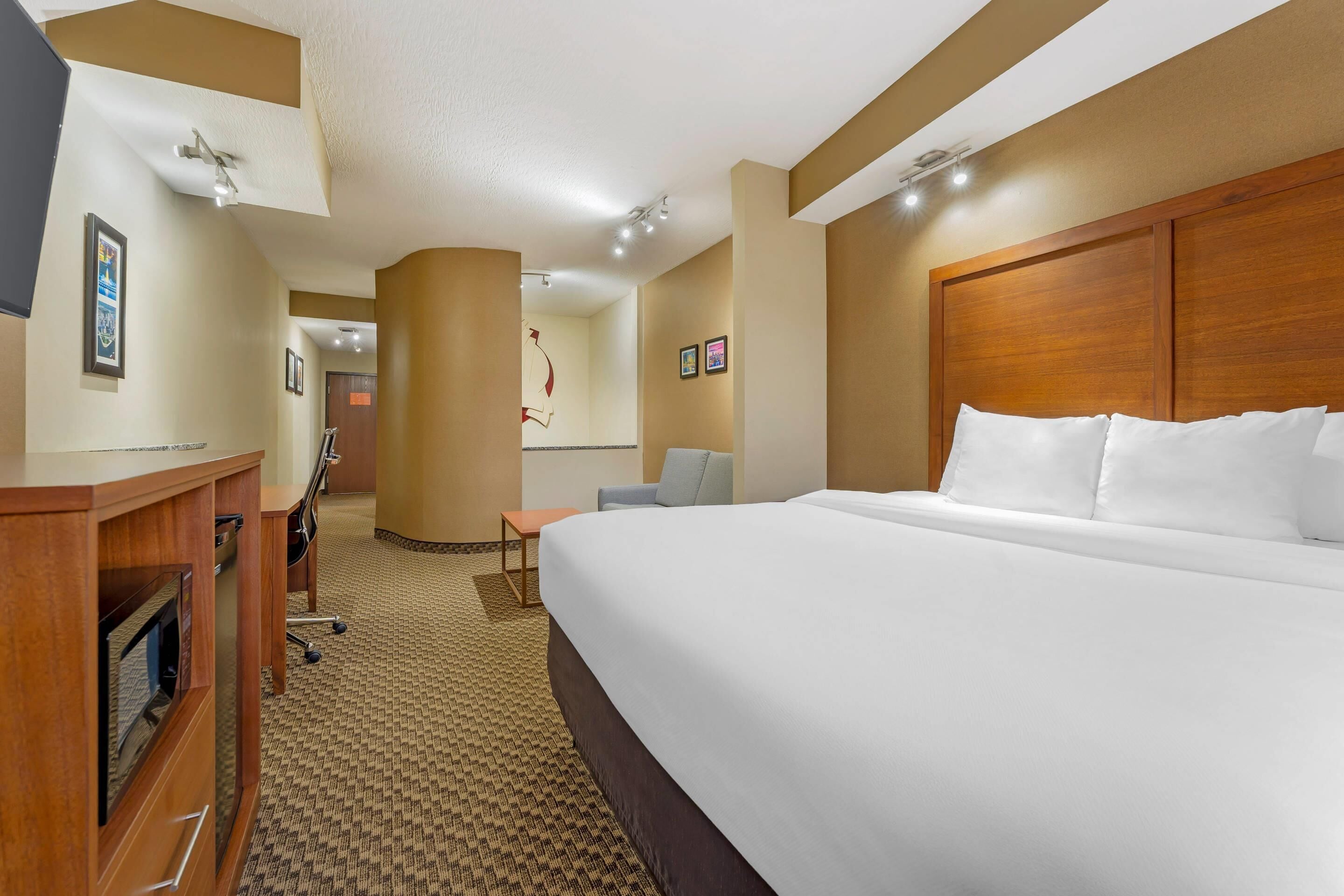 A hotel room with a large bed, a desk with a computer, a chair, and a small table.