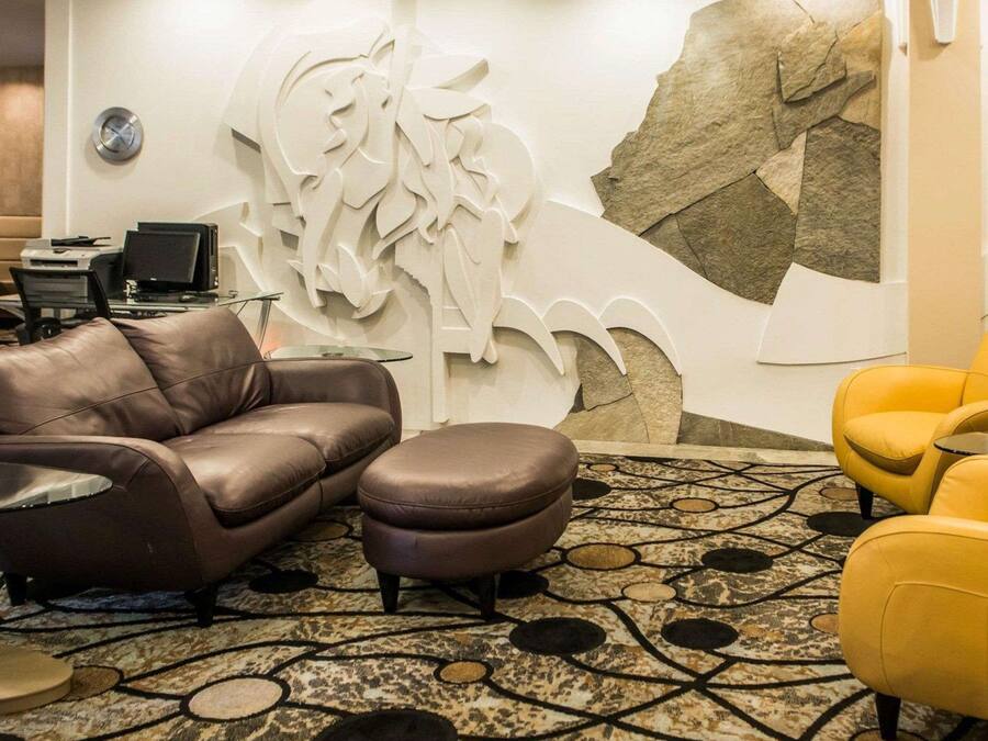 Ein modernes Wohnzimmer mit einem braunen Ledersofa, passendem Hocker und einem gelben Sessel. Ein großes abstraktes Wandbild und eine strukturierte Wand im Stein-Look sind zu sehen.