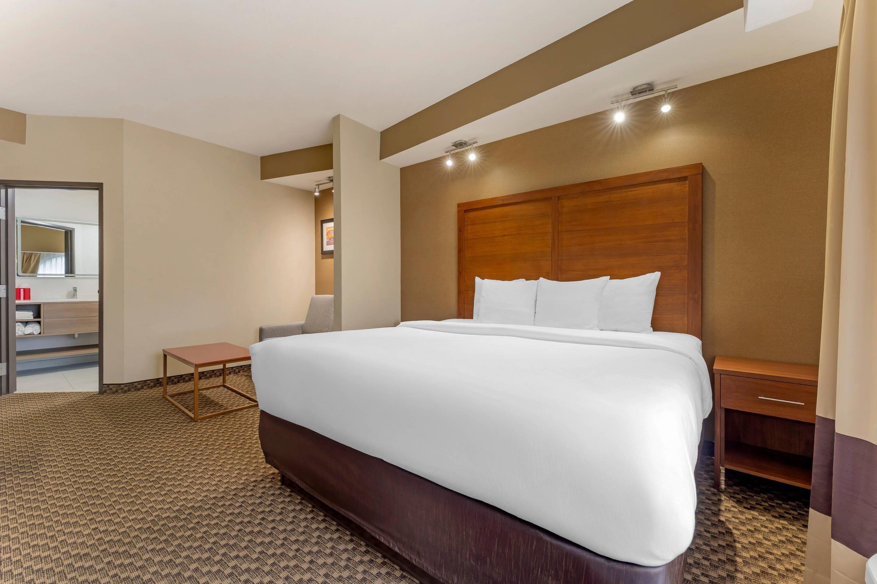 A hotel room with a large bed, a wooden headboard, a small table, a nightstand, and a mirror.