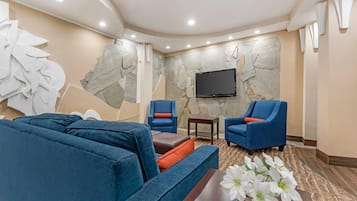 Ein modernes Wohnzimmer mit einer Eckcouch, zwei Sesseln, einem Couchtisch und einem Flachbildfernseher, der an einer strukturierten Wand angebracht ist.