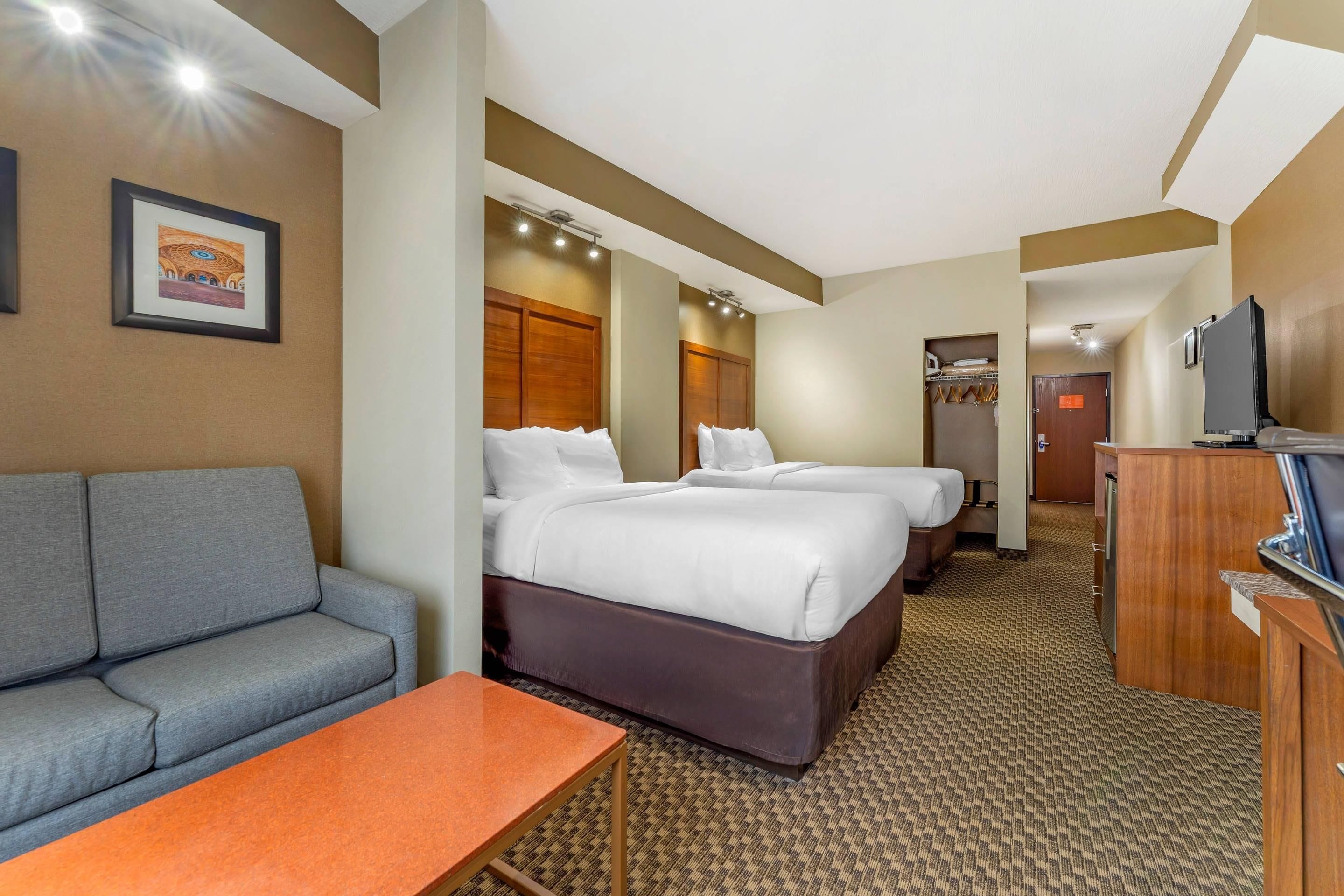 Habitación de hotel con sofá, dos camas, televisión y baño a la vista.