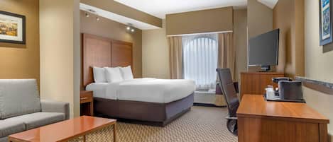 Een hotelkamer met een bed, een bureau, een stoel, een bank, een televisie en een raam met gordijnen.