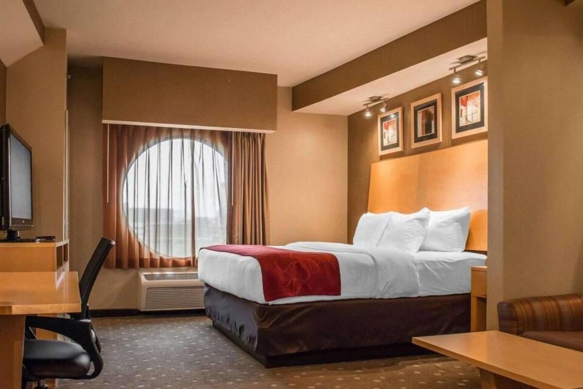 A hotel room with a bed, a desk, a chair, a TV, and a large window with curtains.