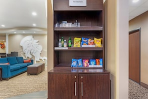 A hotel lobby with a blue sofa, a large abstract wall art, and a beverage vending machine. - Comfort Suites Monroeville - Pittsburgh East (Monroeville)