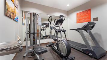 Un gimnasio con equipo de cardio, una máquina de pesas y un espejo grande.